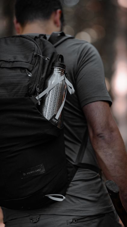 hiker with water bottle in backpack side pocket on a trail