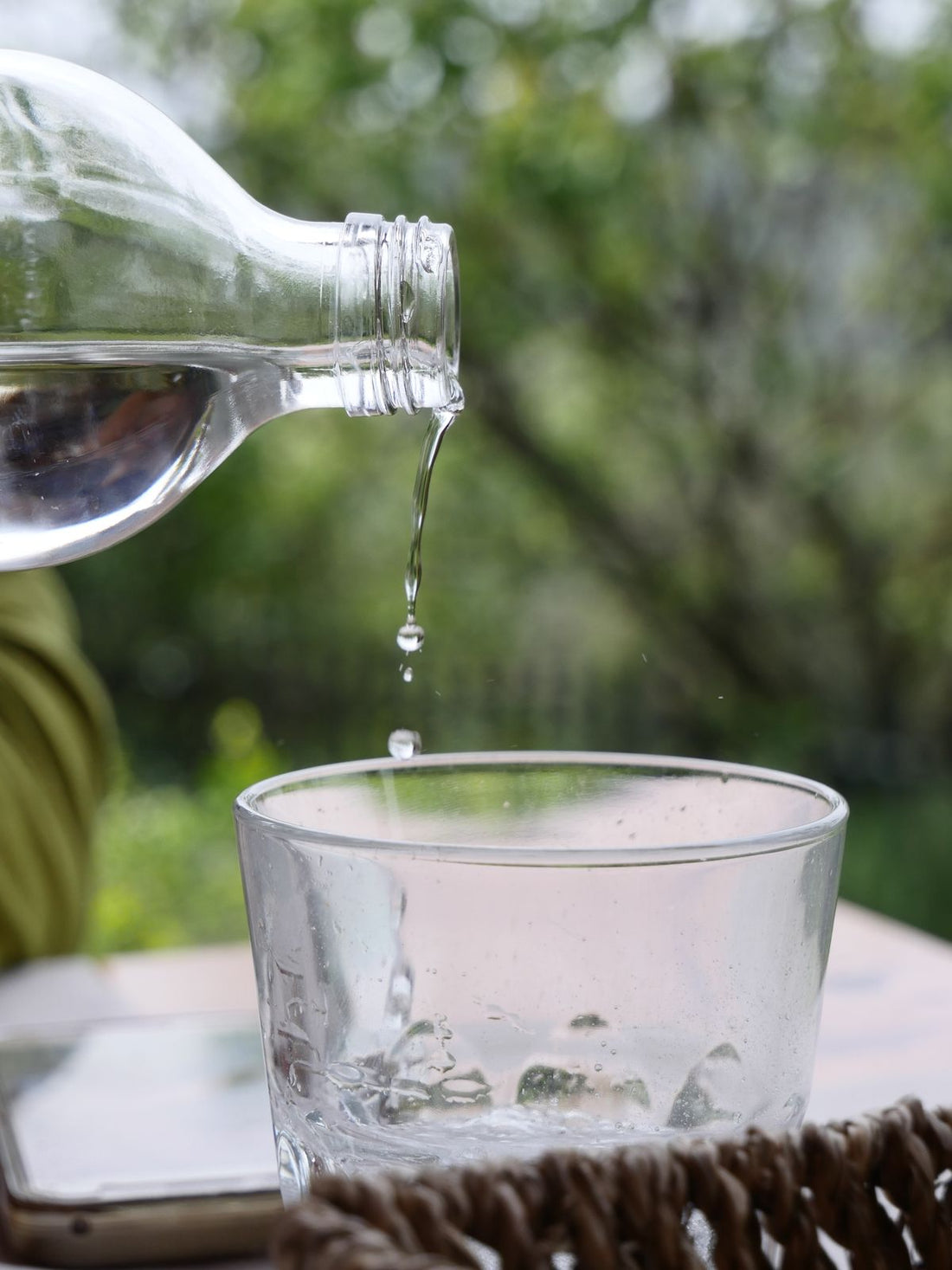 pouring fresh water from a bottle into a glass outdoors to make hiking water taste better