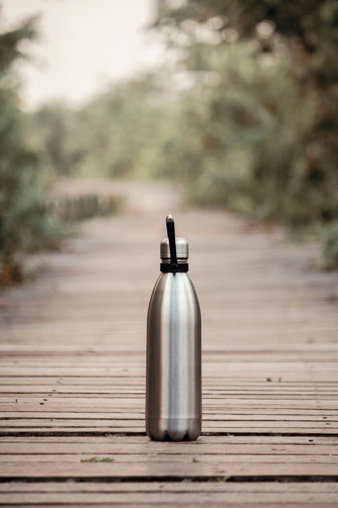 stainless steel reusable water bottle on a wooden dock outdoors, worn from years of use