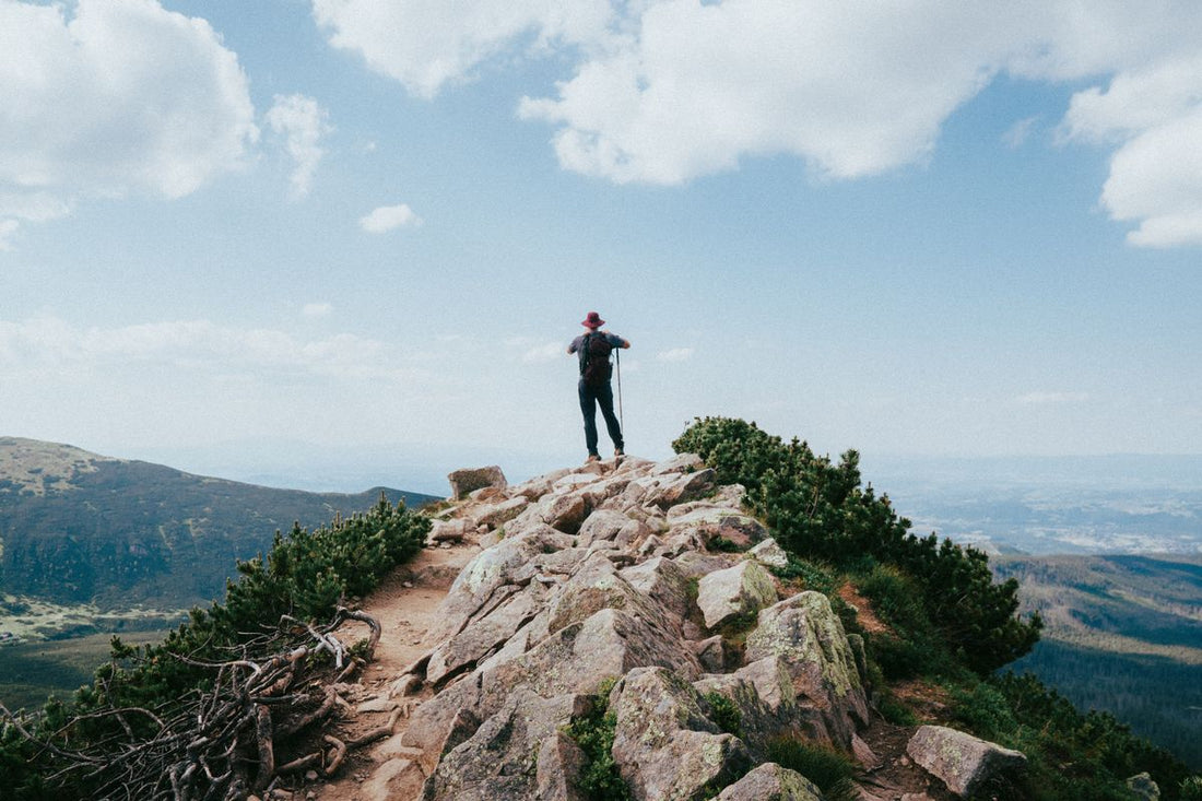 hiker on top of a rocky mountain summit conserving water on a dry exposed trail
