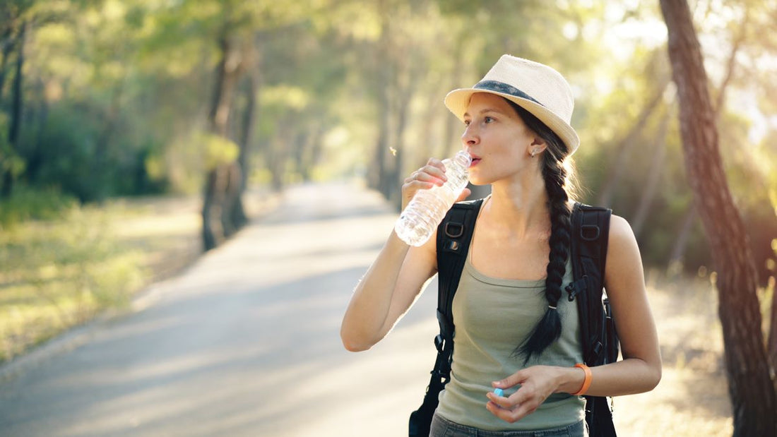 woman drinking water from a bottle on a forest hiking trail