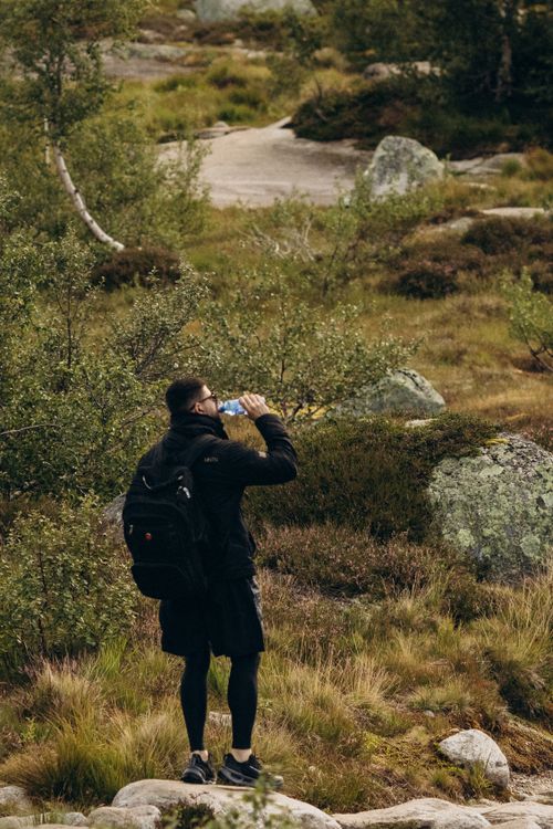 hiker drinking water from an insulated water bottle on a summer mountain trail