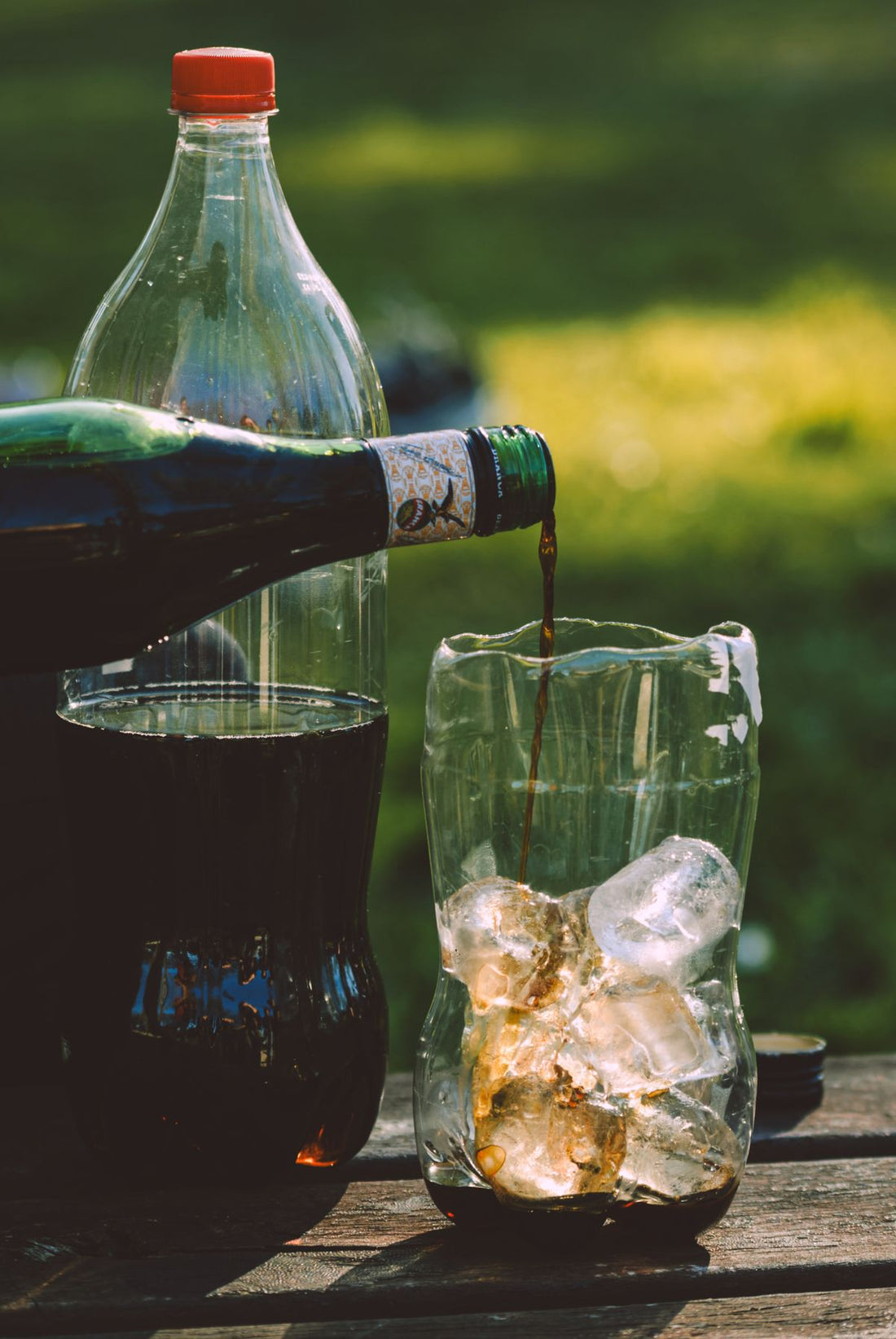 pouring a cold drink over ice cubes outdoors at a picnic table on a sunny day