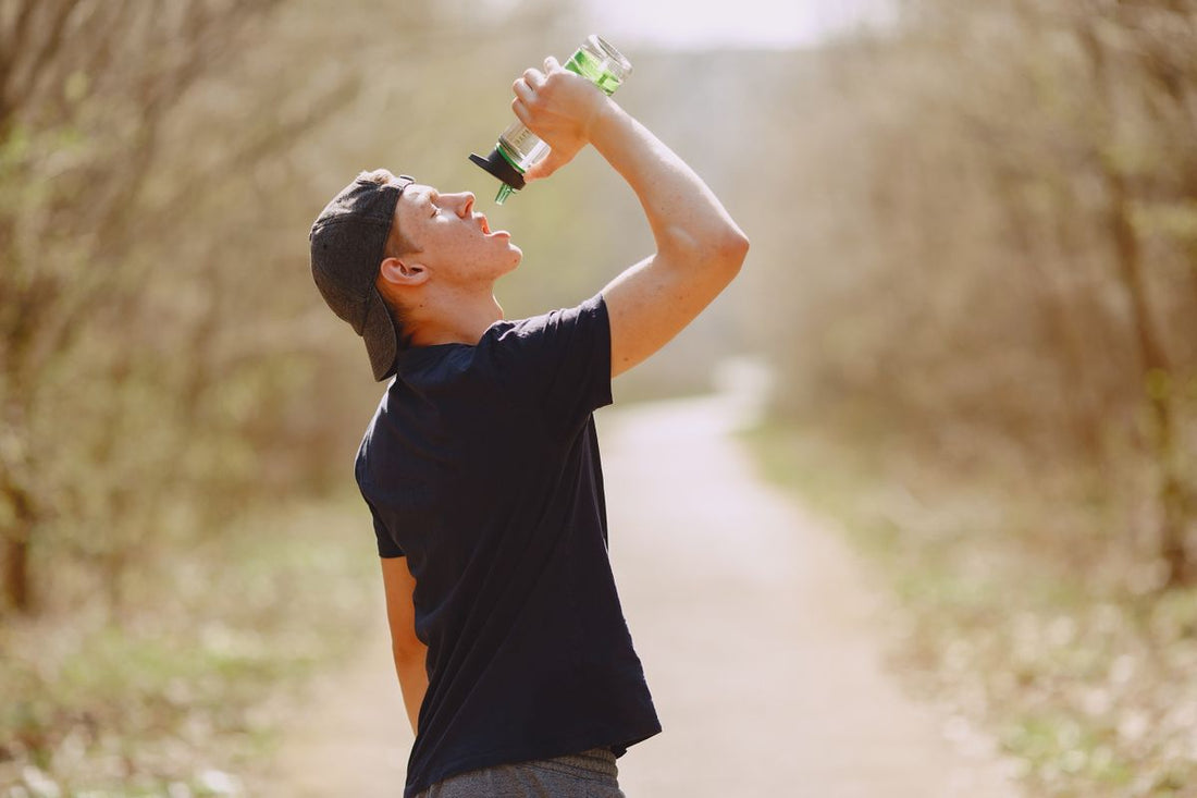 runner drinking water from a bottle on a sunlit trail during a run