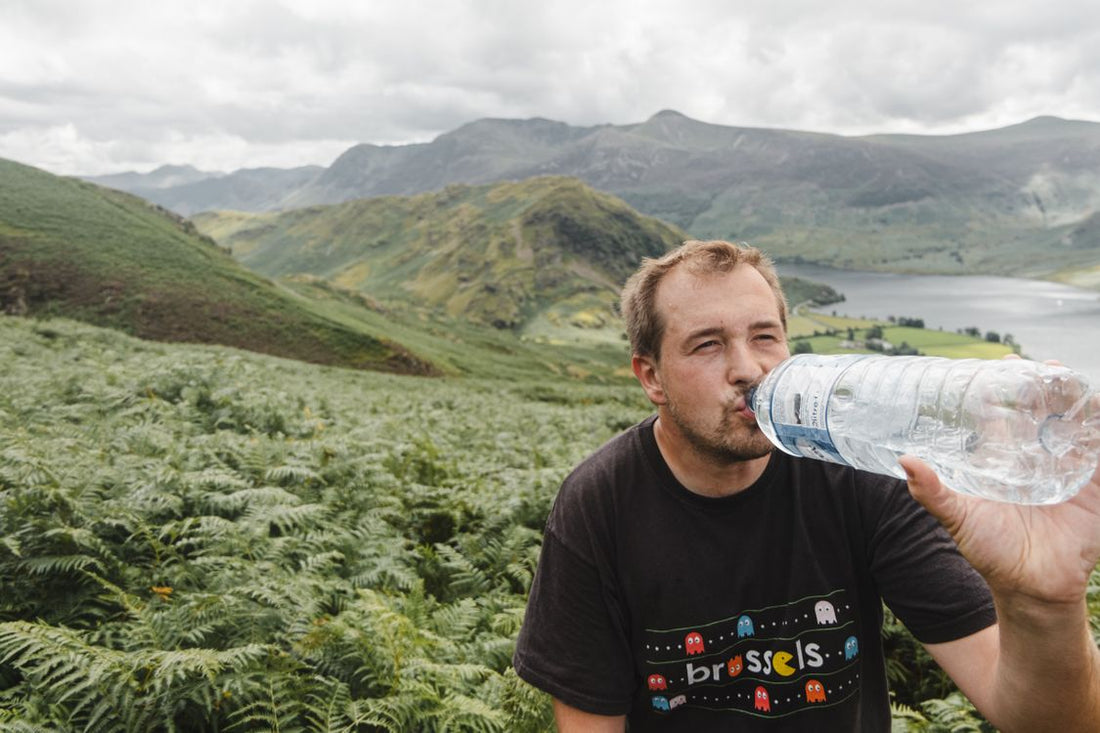 hiker drinking water from a bottle on a lush mountain trail