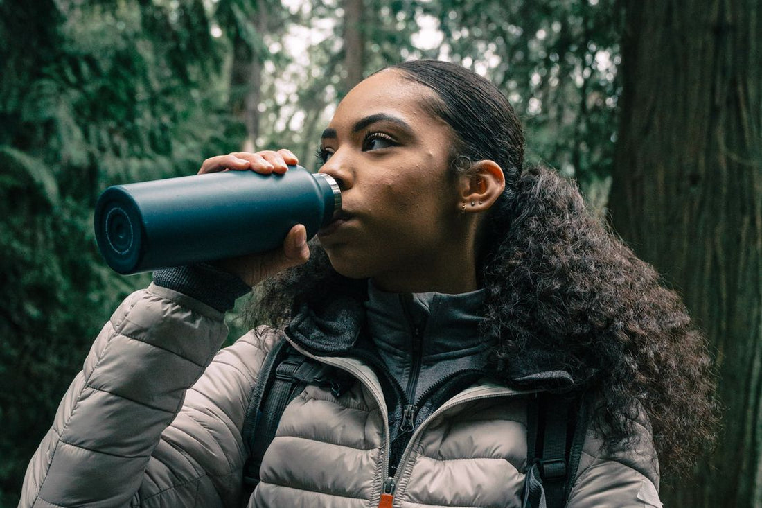 hiker drinking water from a bottle on a forest trail while planning water stops