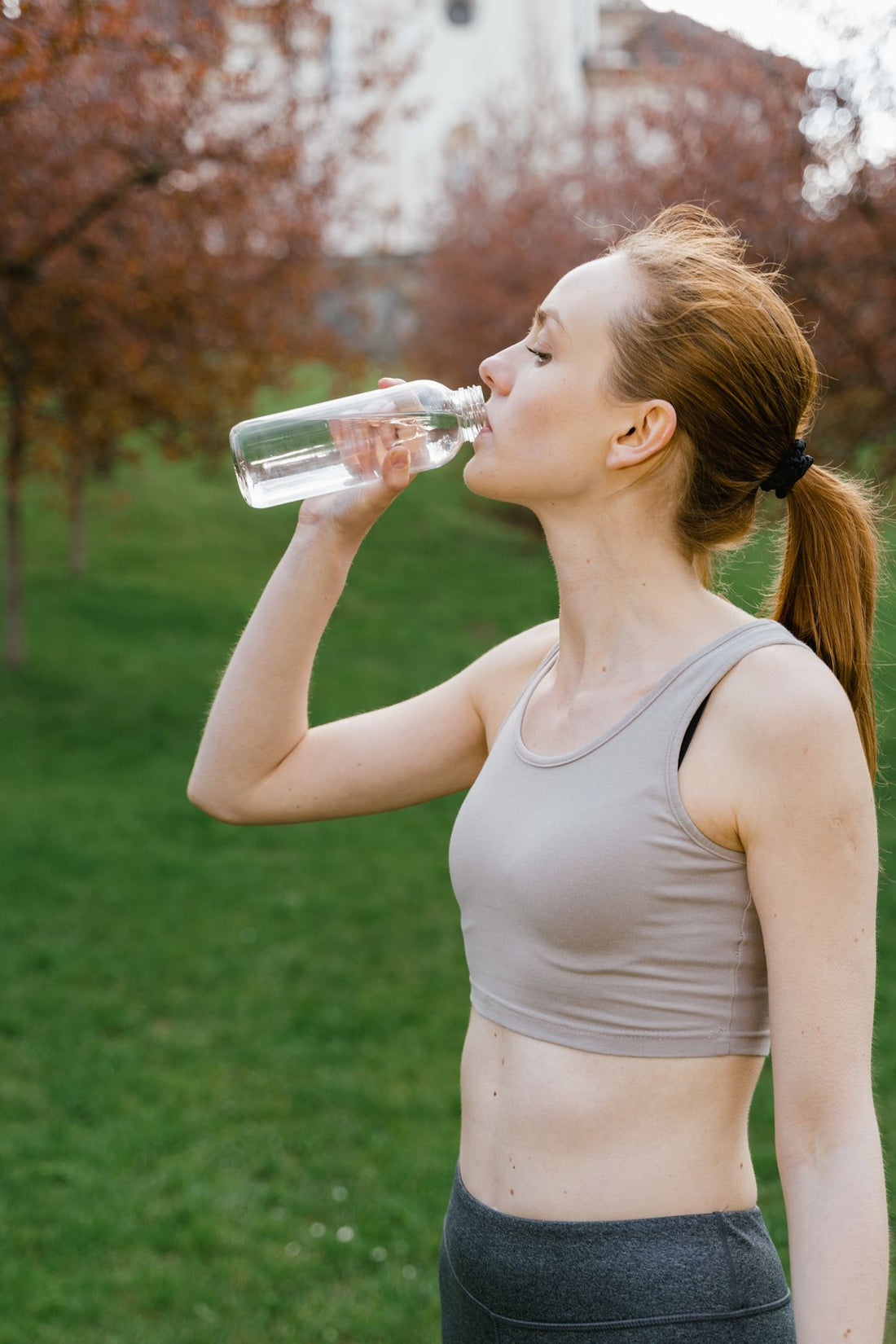 woman drinking water from a reusable bottle outdoors to drink more water every day