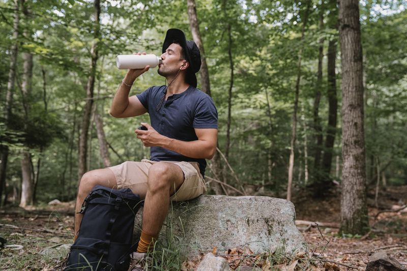 hiker drinking water from insulated bottle while resting on a forest trail