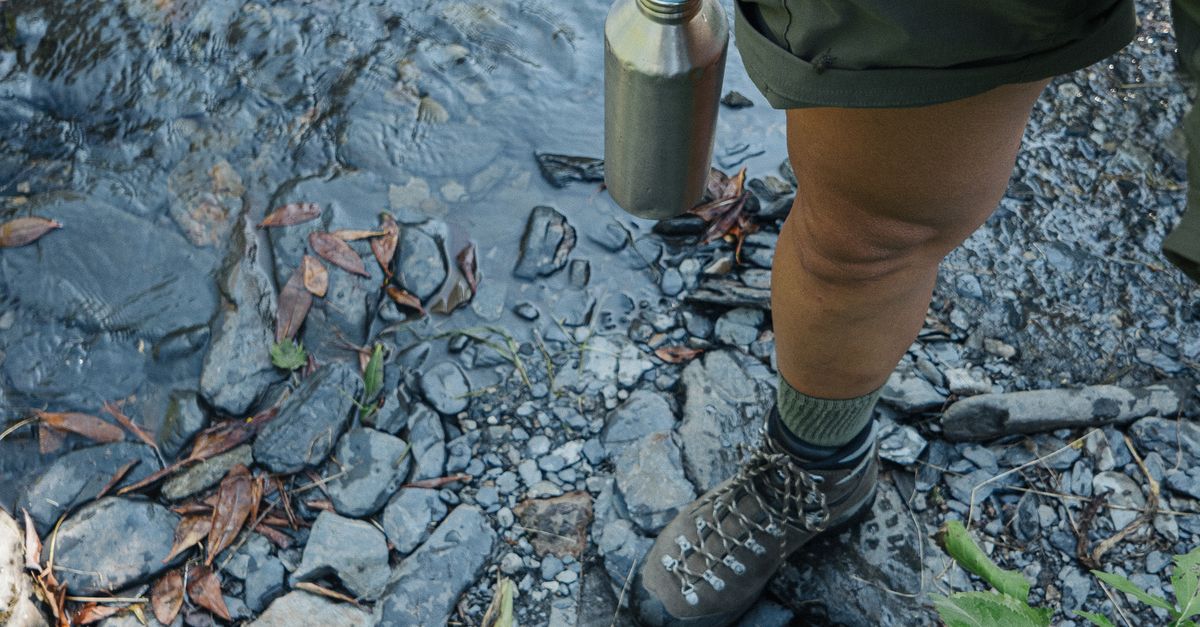 hiker filling water bottle from clear mountain stream while hiking