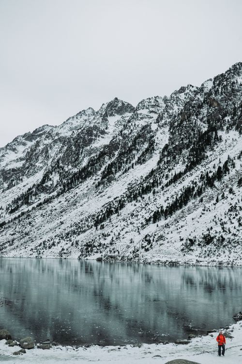 hiker in red jacket standing by a frozen lake with snow-covered mountains, winter hiking hydration