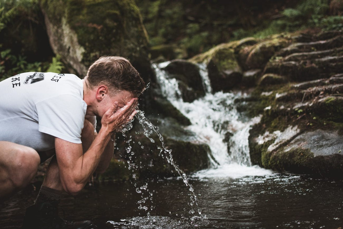 hiker cooling off with cold stream water on a hiking trail to stay hydrated